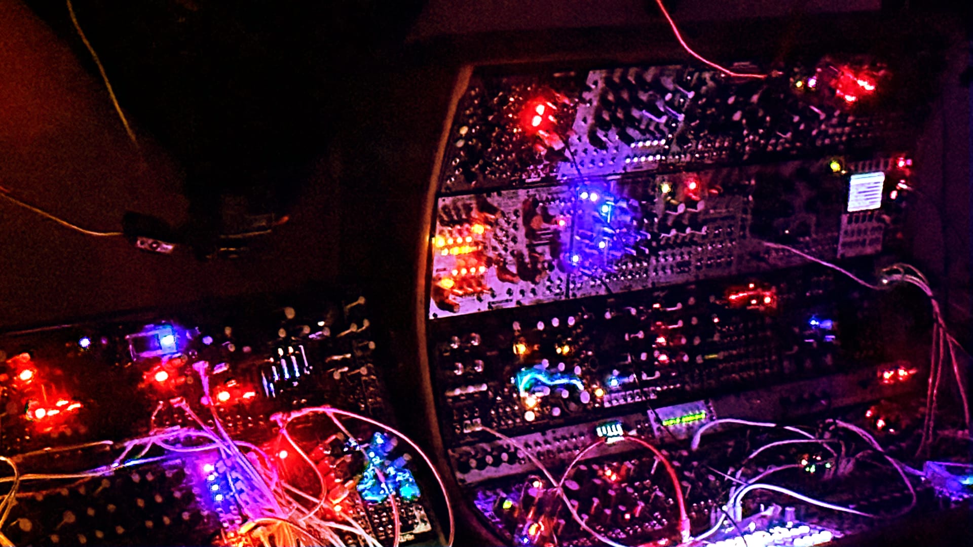 Dark room image of modular synth glowing LEDs