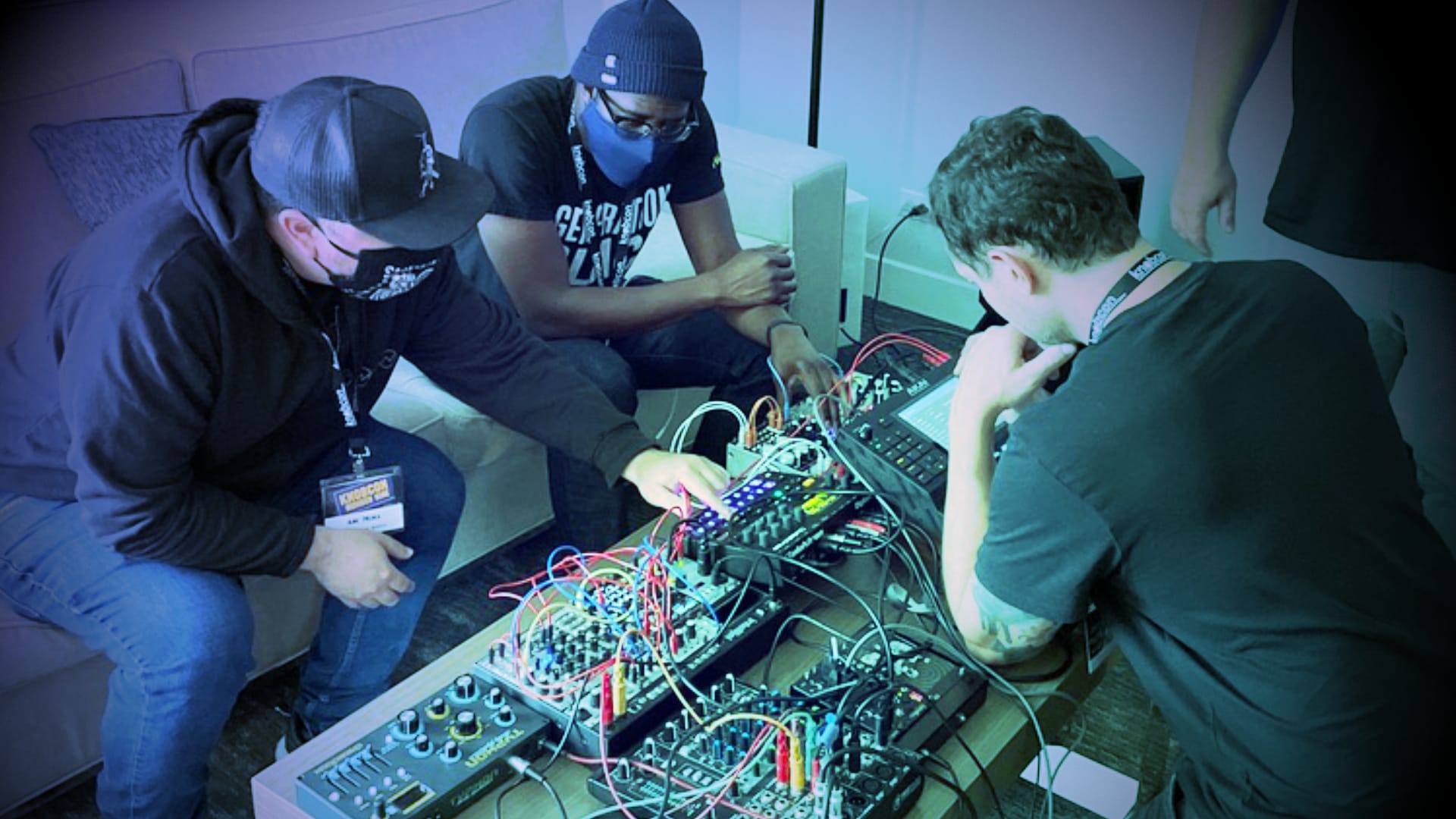 Three people sitting around a coffee table covered in modular synths.